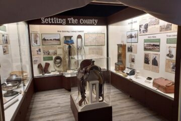A photo showing a museum exhibit with large title "settling the county" and ranching gear on display.