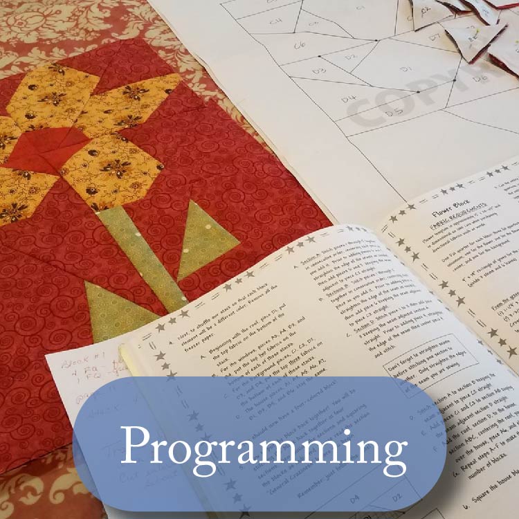 An image of a quilt in progress showing cut pieces, a shown section that looks like a flower, and an open book. Button reads "programming" 