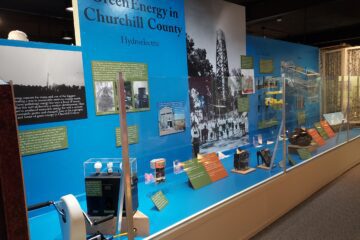 A photograph of the museum exhibit, featuring objects, panels, photographs, and a massive image of steam erupting from an oil derrick