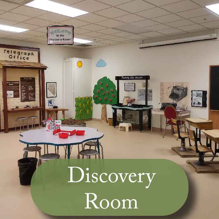 Photo of hands on activities featuring a craft table, fake crops, typewriter, and others. Button at the bottom reads "discovery room" 